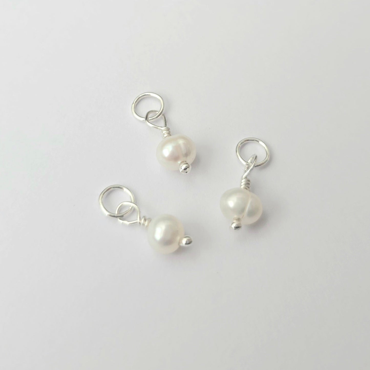 Three pearl charms on silver loops against a light gray background