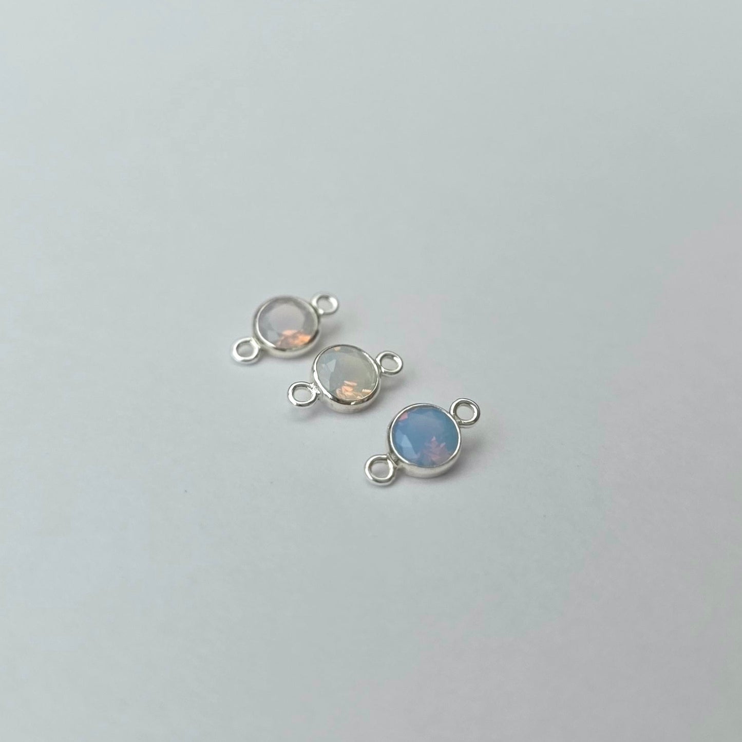 Three silver jewelry connectors with gemstones on a light gray background