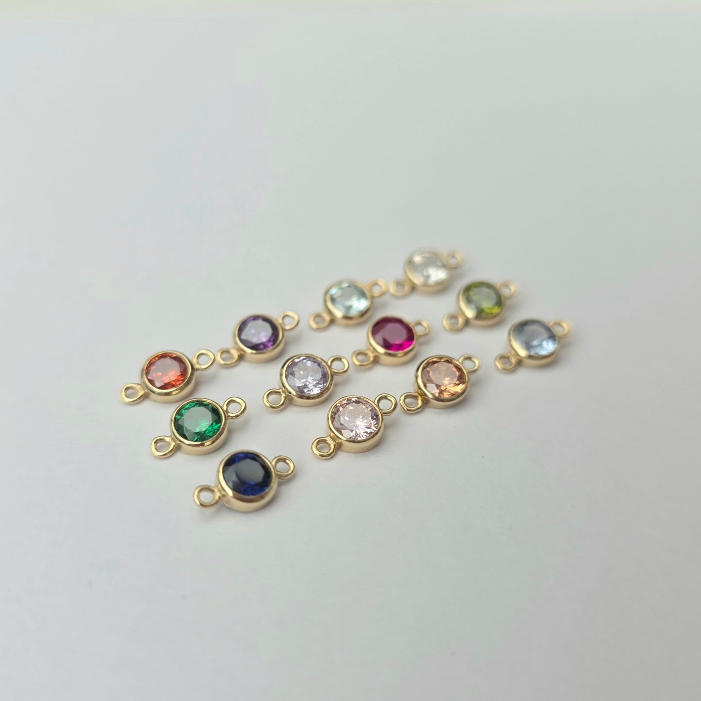Gold jewelry connectors with colorful gemstones on a light gray background