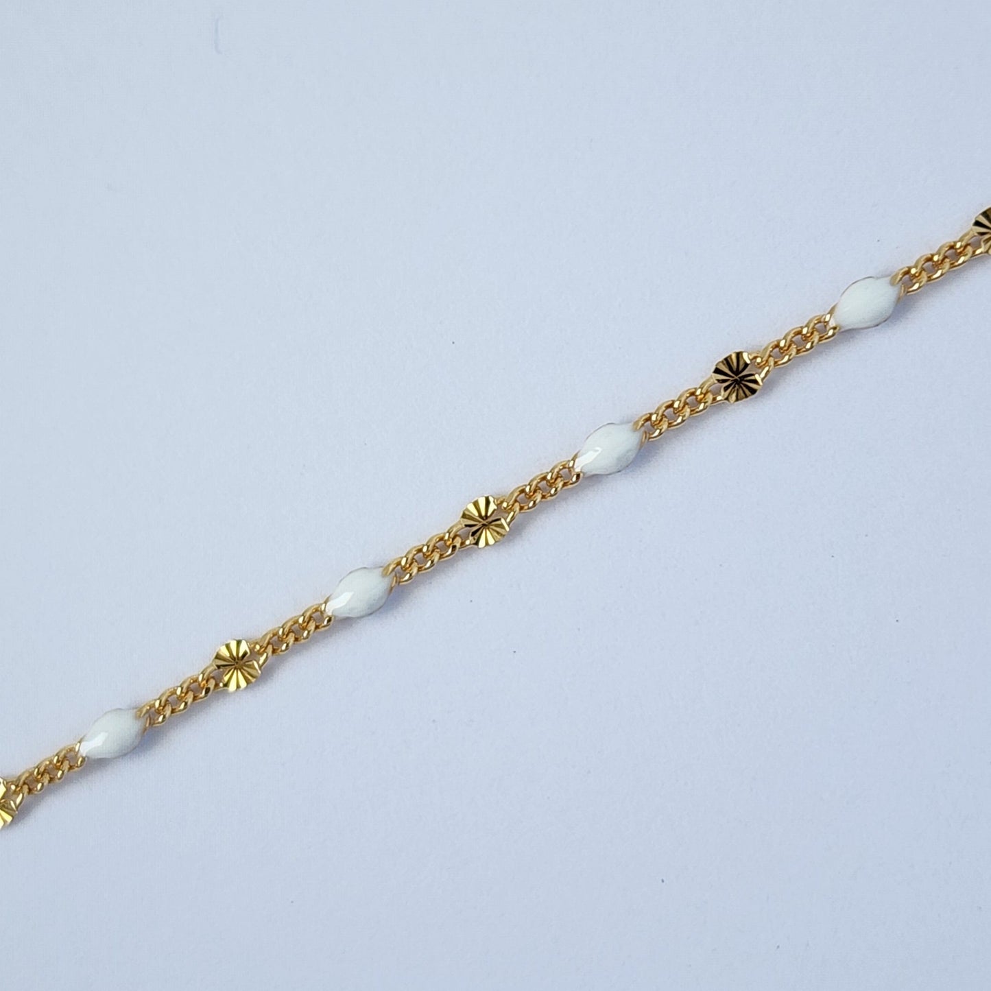 Gold bracelet with white beads on a light gray background