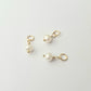 Three pearl charms with gold loops on a light gray background