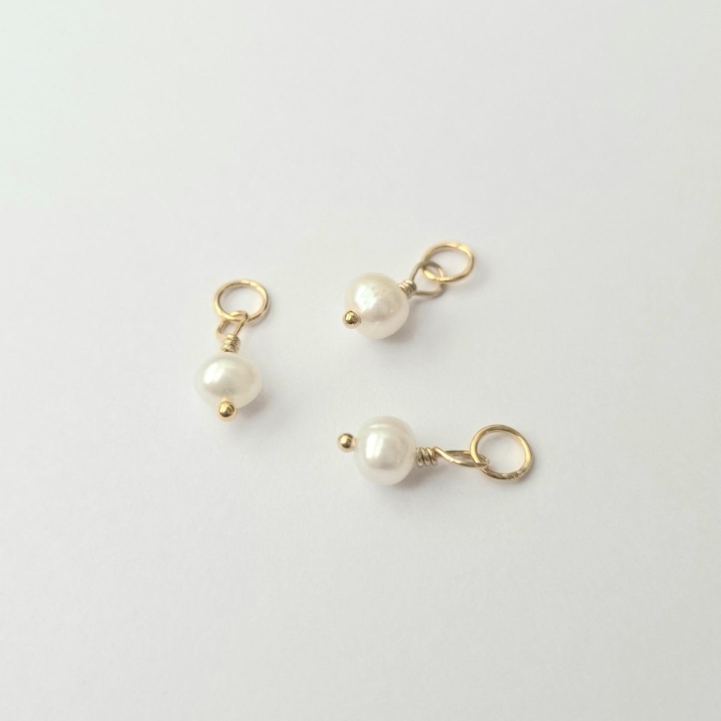 Three pearl charms with gold loops on a light gray background