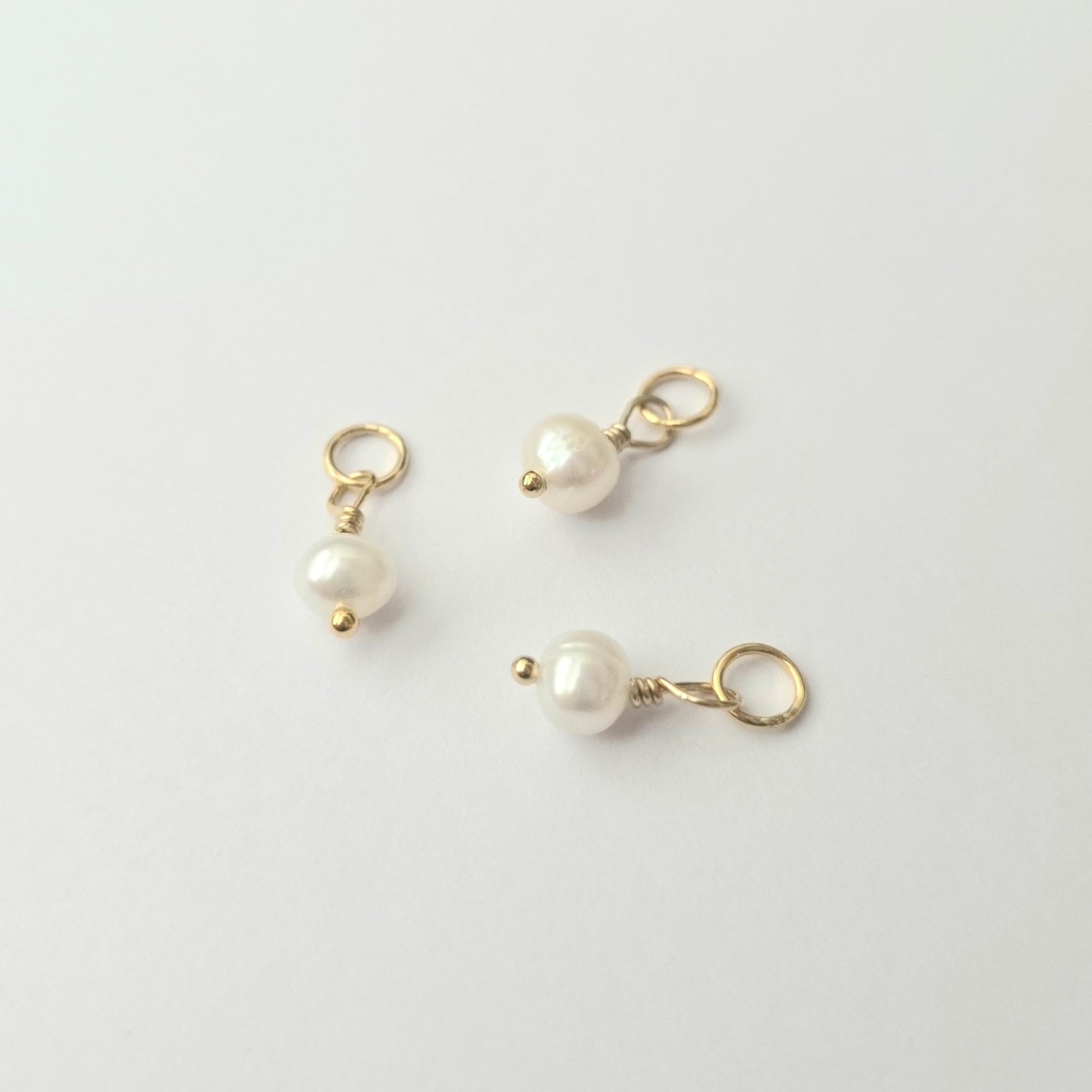 Three pearl charms with gold loops on a light gray background