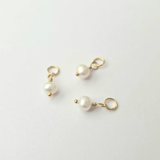 Three pearl charms on gold loops against a white background