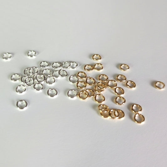 A collection of silver and gold filled jump rings arranged on a white surface.