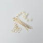 Gold jewelry-making components including pins, rings, and pearls on a light gray background