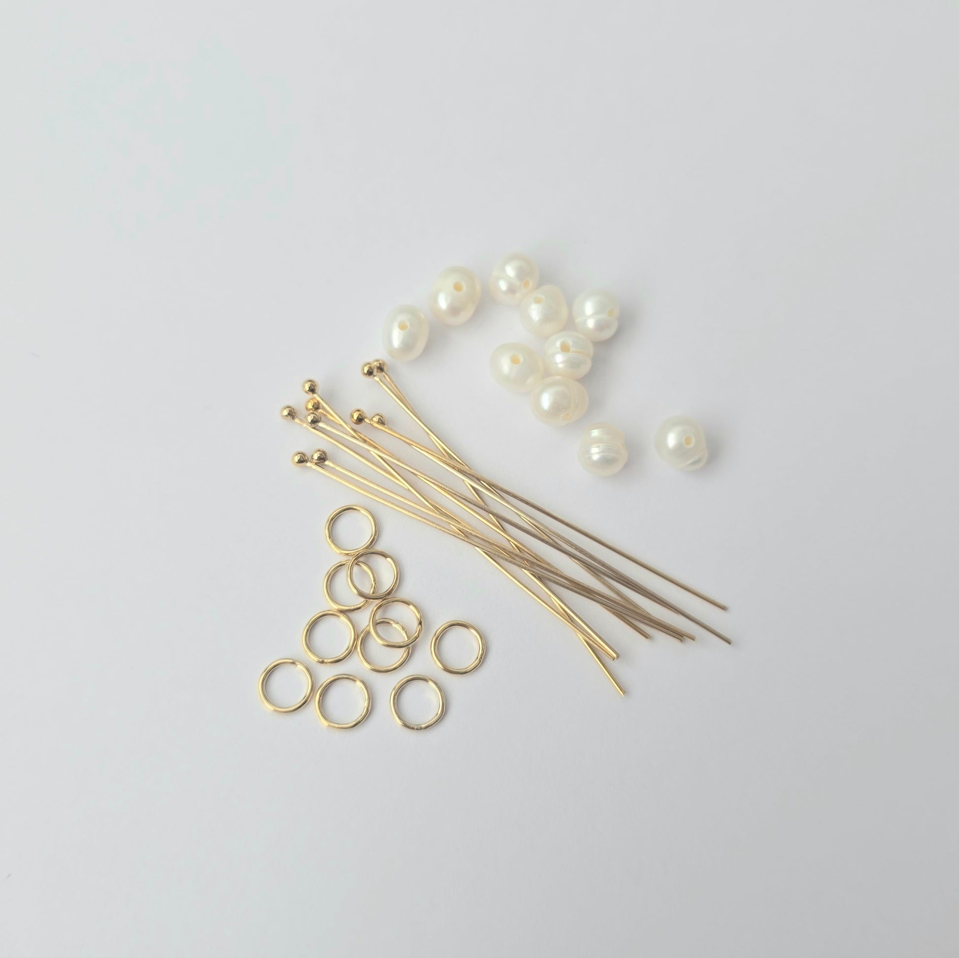 Gold jewelry-making components including pins, rings, and pearls on a light gray background