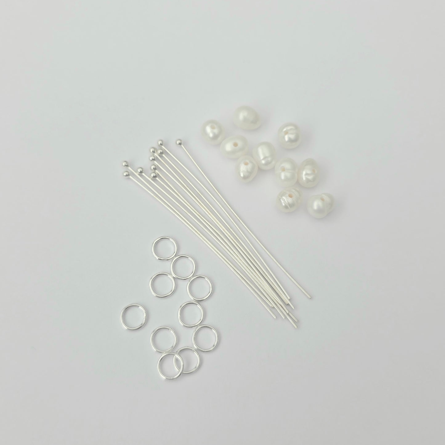Jewelry-making supplies including silver jump rings, wires, and pearls on a light gray background