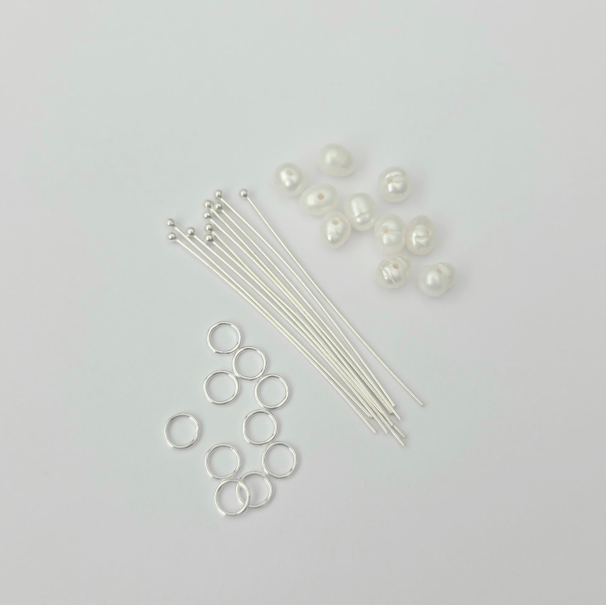 Jewelry-making supplies including silver jump rings, wires, and pearls on a light gray background