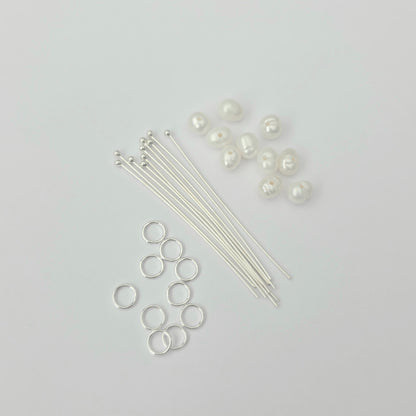 Jewelry-making supplies including silver jump rings, wires, and pearls on a light gray background