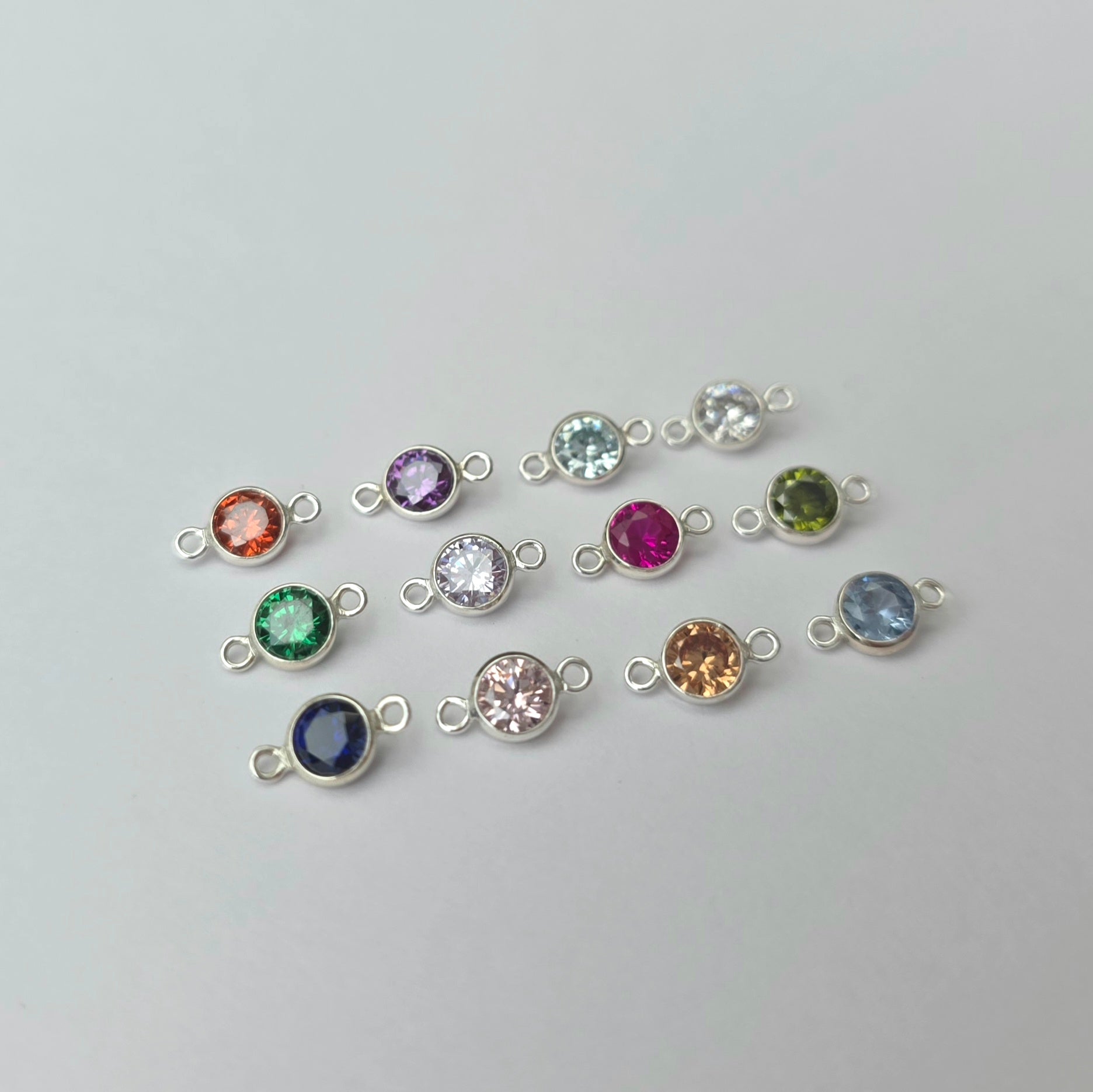 Silver jewelry connectors with colorful gemstones on a light gray background