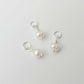 Three pearl charms on silver loops against a light gray background