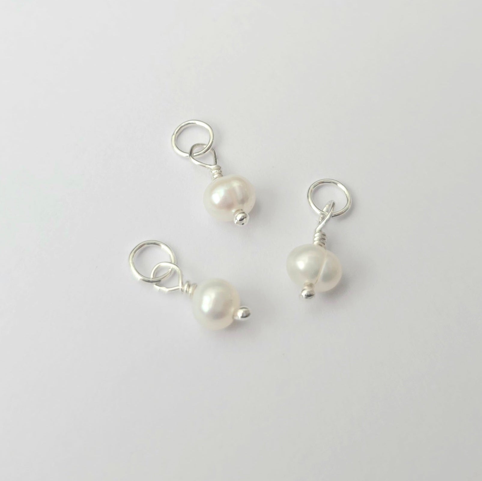 Three pearl charms on silver loops against a light gray background
