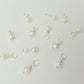 Pearl charms on silver hooks scattered on a light gray background