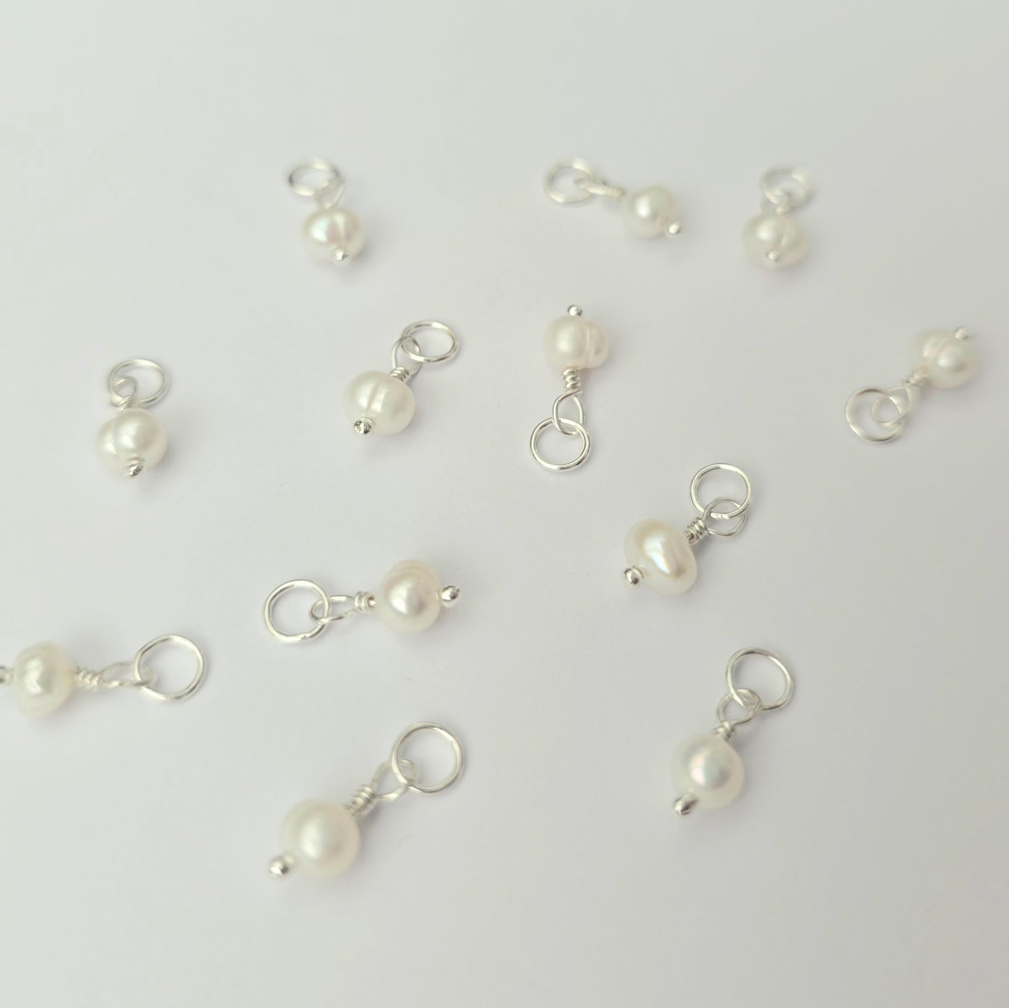 Pearl charms on silver hooks scattered on a light gray background