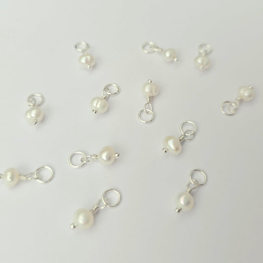 Pearl charms on silver hooks scattered on a light gray background