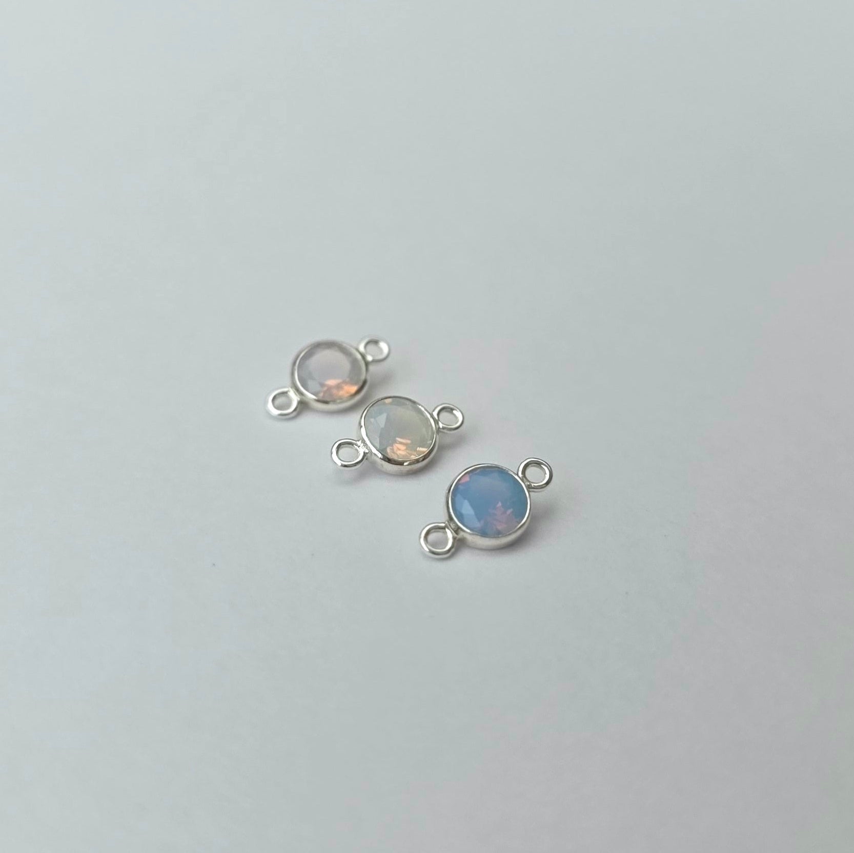 Three silver jewelry connectors with gemstones on a light gray background