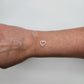 Silver heart-shaped charm on a wrist against a neutral background